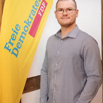 Der Beisitzende Alexander Schnurbus or einem Fachwerk Hintergrund neben einem Aufsteller mit FDP-Logo